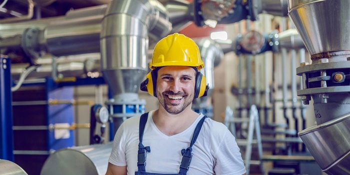 Ein Mann mit Arbeitskleidung, Bauhelm und Gehörschutz